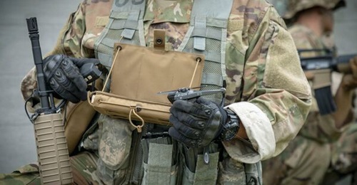 A Black Hornet ready to launch, with the monitor attached to a combat flack vest. The operator is holding the Black Hornet 3 controller.