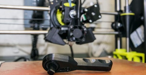 A 3D-printed ratchet sits on the board of a LulzBot Taz 6 3D printer aboard USNS 
        
         (T-AKE 2) in support of an additive manufacturing test phase.