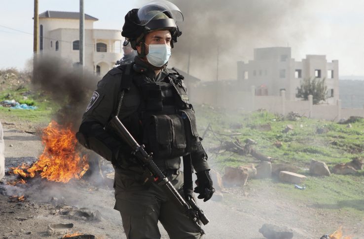 An Israeli security guard stands by burning tyres amid clashes with Palestinian protesters following their demonstration against the expansion of settlements in the town of Salfit, in the Israeli-occupied West Bank, on 4 December 2020. Public unrest in the West Bank will remain a major challenge as security co-operation between Israel and the Palestinian Authority resumes. (Jaafar Ashtiyeh/AFP via Getty Images)