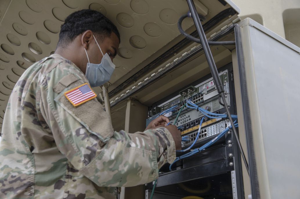 A US Army specialist with the 1st Armored Division Combat Aviation Brigade uses a Category 5 cable to establish a network connection at Camp Atterbury Joint Maneuver Training Center in Indiana. (US Army )